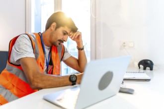 Young construction worker feeling stressed while working remotely from home using laptop, having
