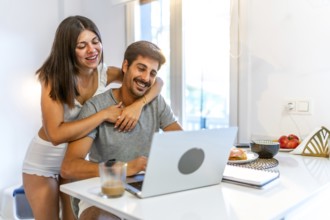 Young couple embracing and enjoying each other's company while working on a laptop in a cozy