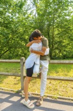 Romantic couple hugging near a wooden fence in a park, enjoying a sunny summer day surrounded by