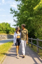 Young couple strolls along a paved path beside a road, enjoying each other's company on a sunny day
