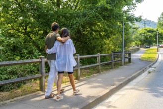 Romantic couple walking on a paved path in a park, embracing each other, enjoying a sunny summer