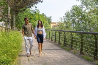 Happy couple enjoying a leisurely stroll, holding hands and walking along a paved path in a green