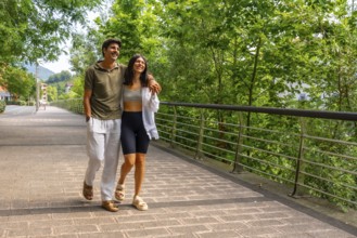 Young couple enjoying a leisurely stroll across a bridge in a green park, embracing the tranquility