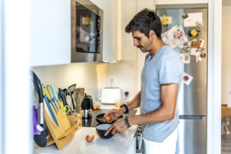 Young man cracking eggs into a bowl, preparing to cook breakfast or a meal in his modern, well
