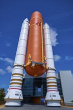 Large orange space shuttle with booster rockets in front of a modern building, Kennedy Space Center