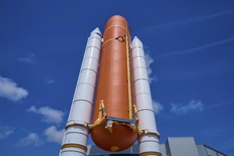 Large orange space shuttle with two launch vehicles against a blue sky, Kennedy Space Center