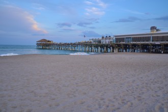 A sandy beach with a pier jutting into the blue sea under a slightly cloudy sky, Westgate Cocoa