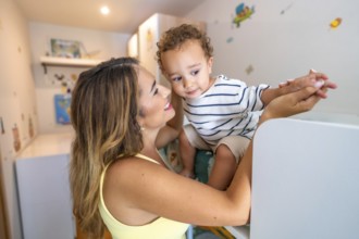 Smiling mother holding hands with her baby son while playing in a decorated children's bedroom