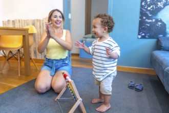 Mother encouraging her baby boy to walk, clapping hands in living room, promoting child development