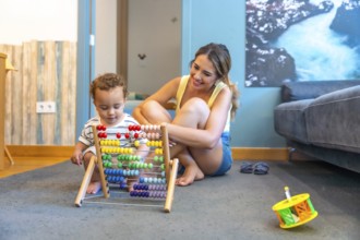 Happy mother watching her baby boy playing with a colorful abacus, developing early math skills in