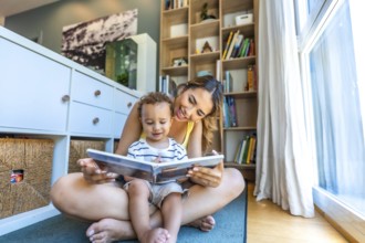 Happy mother and son enjoying quality time together, reading a book on the floor of their cozy