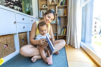 Happy mother and her little son reading a book together, sitting on the floor in the living room