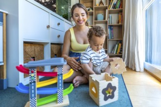 Smiling mother watching her cute toddler son playing with a shape sorter toy and a colorful car
