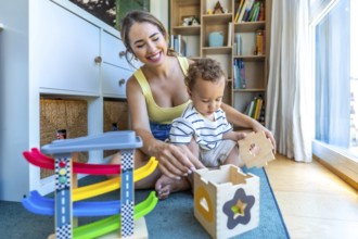 Happy mother and son are sitting on the floor playing with a wooden shape sorter and colorful toy