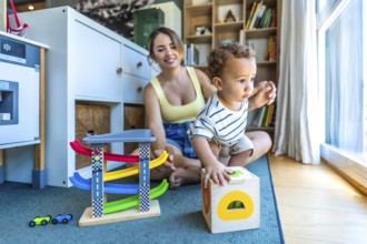 Happy mother watching her toddler son playing with educational wooden toys in a modern living room