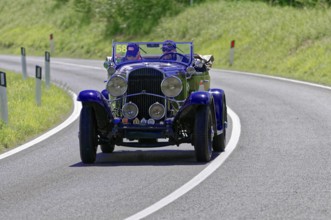 Dark blue classic car on a winding road under a bright sun, classic car, car race, Mille Miglia,