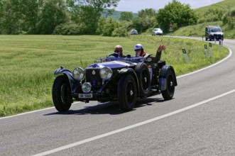 Black classic car with waving driver on winding road in idyllic landscape, classic car, car race,