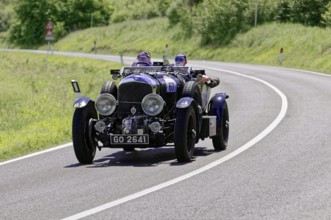 Dark blue classic car with two men on a country road in a green environment, classic car, car race,