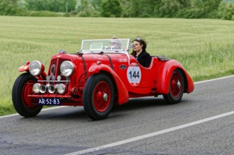 A red vintage car drives with two people through a green landscape, classic car, car race, Mille