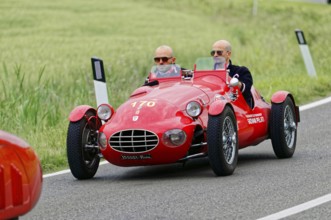 A red sports car with two drivers drives on a rural route, classic car, car race, Mille Miglia,