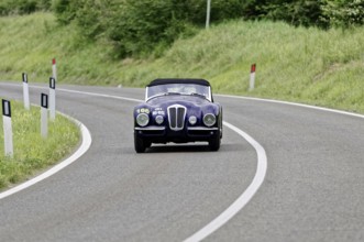 A dark classic car drives alone on a winding country road, classic car, car race, Mille Miglia,