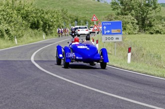 Blue classic car drives towards Siena, accompanied by other vehicles and signs, classic car, car