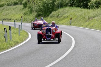 Red classic car in a sharp bend, followed by other classic cars on a country road, classic car, car