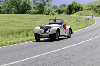 Cream-coloured classic car on a rural road with a green natural backdrop, classic car, car race,