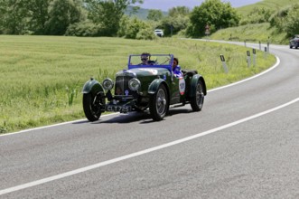 Green classic car drives on a winding country road through a green landscape, classic car, car