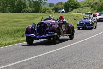 Two classic cars driving with several vehicles on a country road, classic car, car race, Mille
