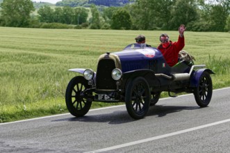 Black vintage car with two men, one waving, on road landscape in spring, vintage car, car race,