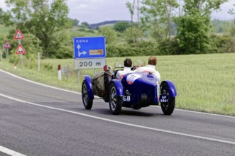 Blue classic car in the direction of Siena on a country road through the Italian countryside,