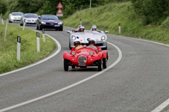 Two people with helmets in a red classic car on a country road, sporty-classic scene, classic car,