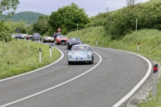 Blue vintage car leads a group of classic cars on a winding country road, picturesque surroundings,