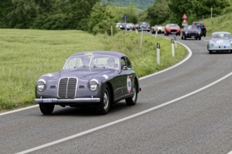 Grey vintage car with race number on a country road, nostalgic atmosphere and historic rally,