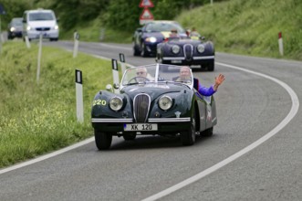 Two people in a green vintage convertible on a winding country road, casual atmosphere, vintage