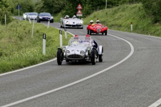 Silver racing car leads ahead of red classic car on winding country road, classic car, car race,