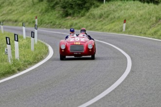 A red convertible sports car with two drivers on a winding country road, classic car, car racing,