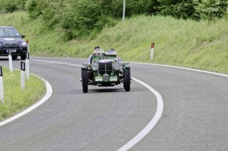 Green vintage car drives on winding country road, lined with green landscape, vintage car, car