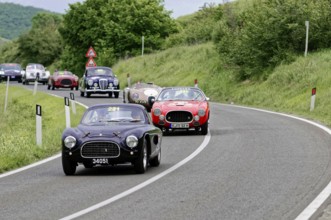 Black classic car followed by red and other classic cars on a winding road, dynamic race, classic