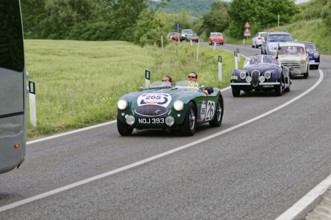 Green classic car in a row of vehicles on a winding country road, classic car, car race, Mille
