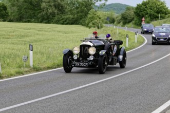 A classic vintage car with two drivers takes part in a car rally on a picturesque road, classic