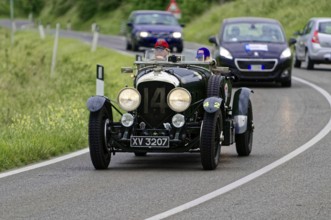 A classic vintage car drives in a rally on a winding country road through green surroundings,
