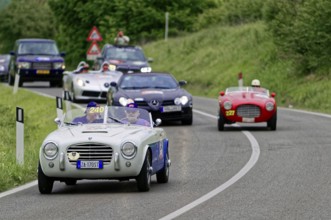 Classic car driving on a winding country road in the middle of a green landscape at a car rally,