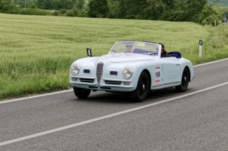 Blue convertible on a country road with green meadows in the background, classic car, car race,