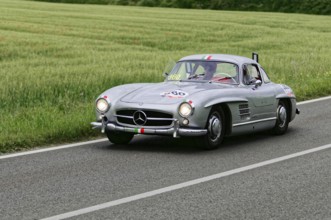 Silver classic car drives along a country road with green fields, classic car, car race, Mille