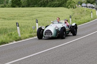 Grey classic car on a country road surrounded by green fields and trees, classic car, car race,