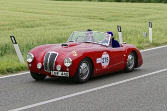 Red classic car on a country road in a vast green environment, classic car, car race, Mille Miglia,