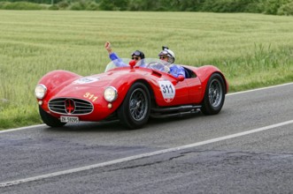 Two people joyfully driving a red Maserati on a country road, classic car, car race, Mille Miglia,