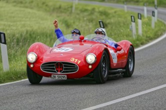 Two people driving in a red Maserati classic car on a winding country road, classic car, car